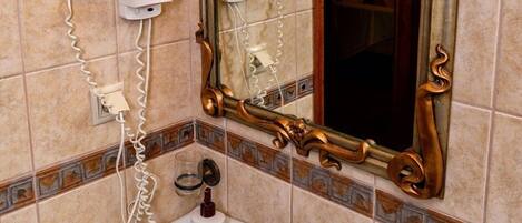 A bathroom with a large ornate mirror, a white sink, and a hairdryer mounted on the wall.
