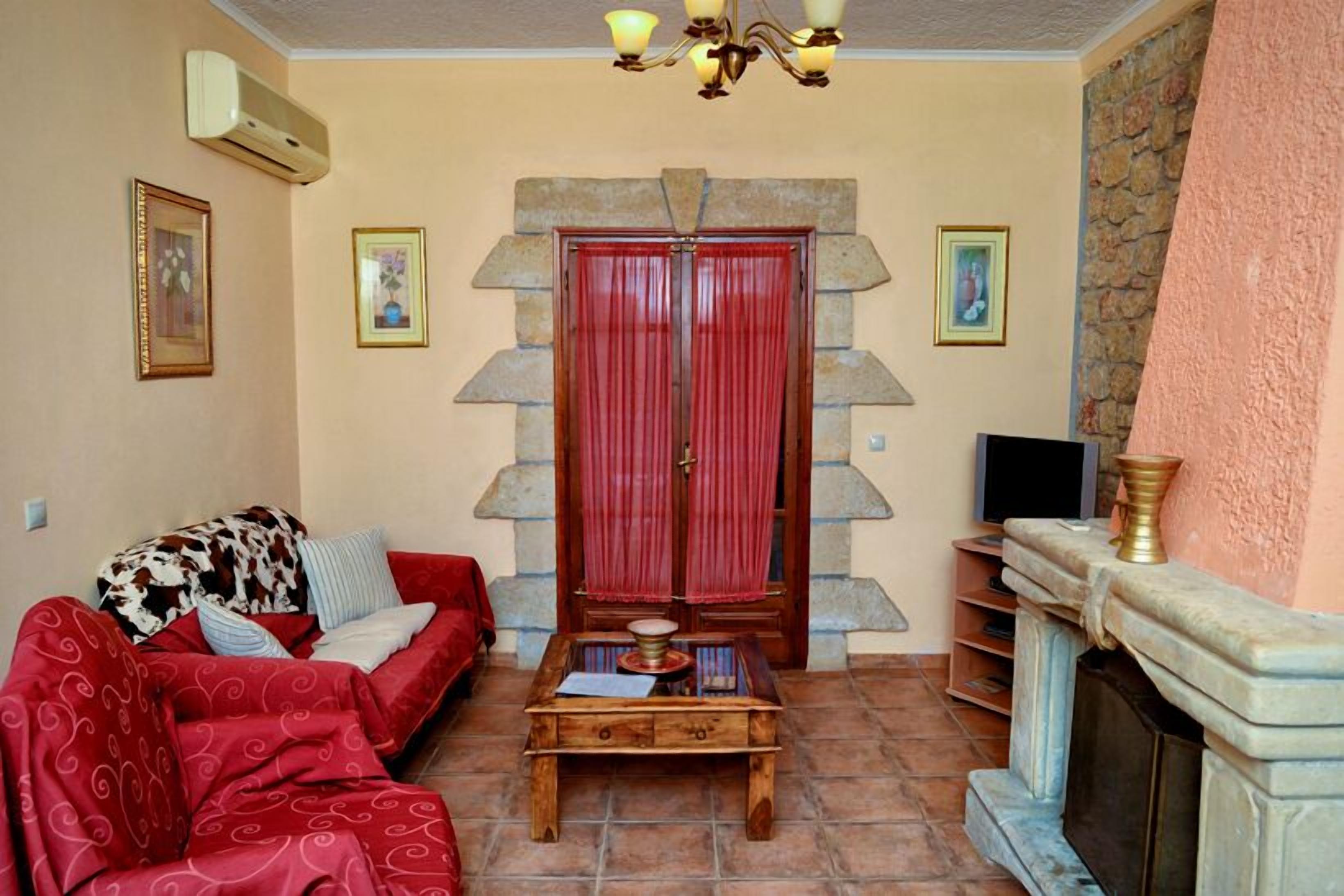 Una sala de estar con un sofá rojo, una mesa de centro de madera, una chimenea de piedra y un arco de piedra con cortinas rojas.