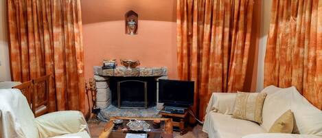 Ein gemütliches Wohnzimmer mit Kamin aus Stein, zwei weißen Sofas, einem Couchtisch und orangefarbenen Vorhängen.