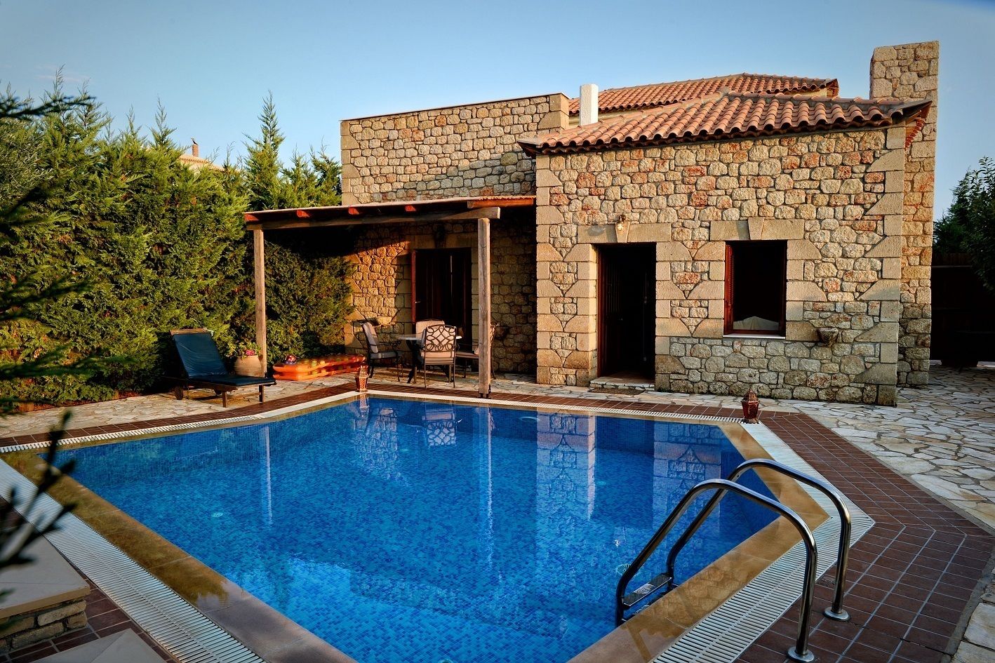 A stone building with a swimming pool, outdoor seating, and a covered patio area.