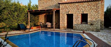 A stone building with a swimming pool, outdoor seating, and a covered patio area.