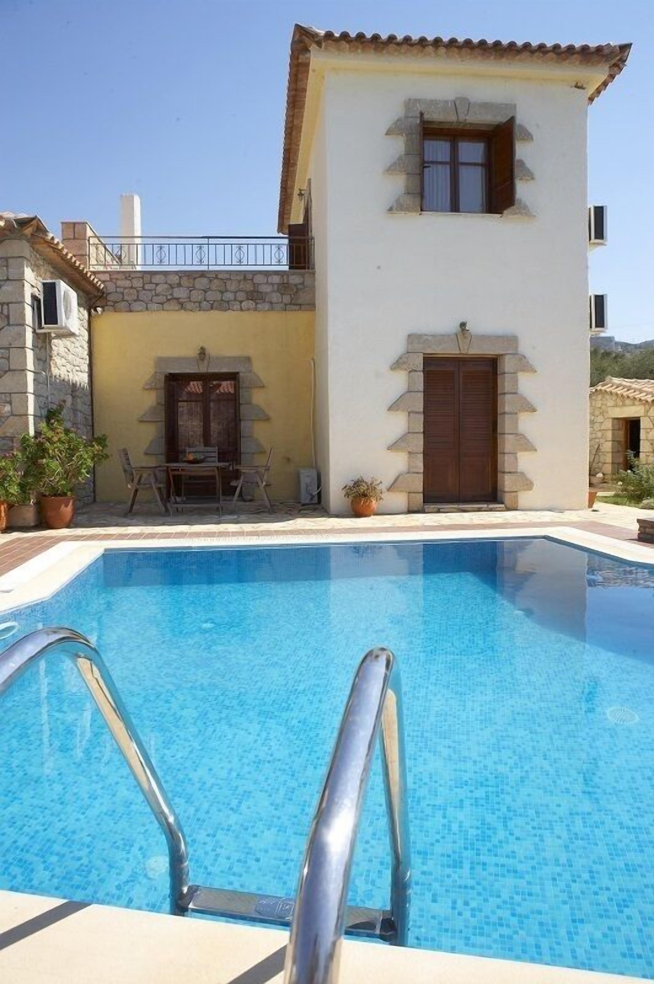 Una piscina con un muro in pietra e un edificio bianco con una porta e una finestra marroni.