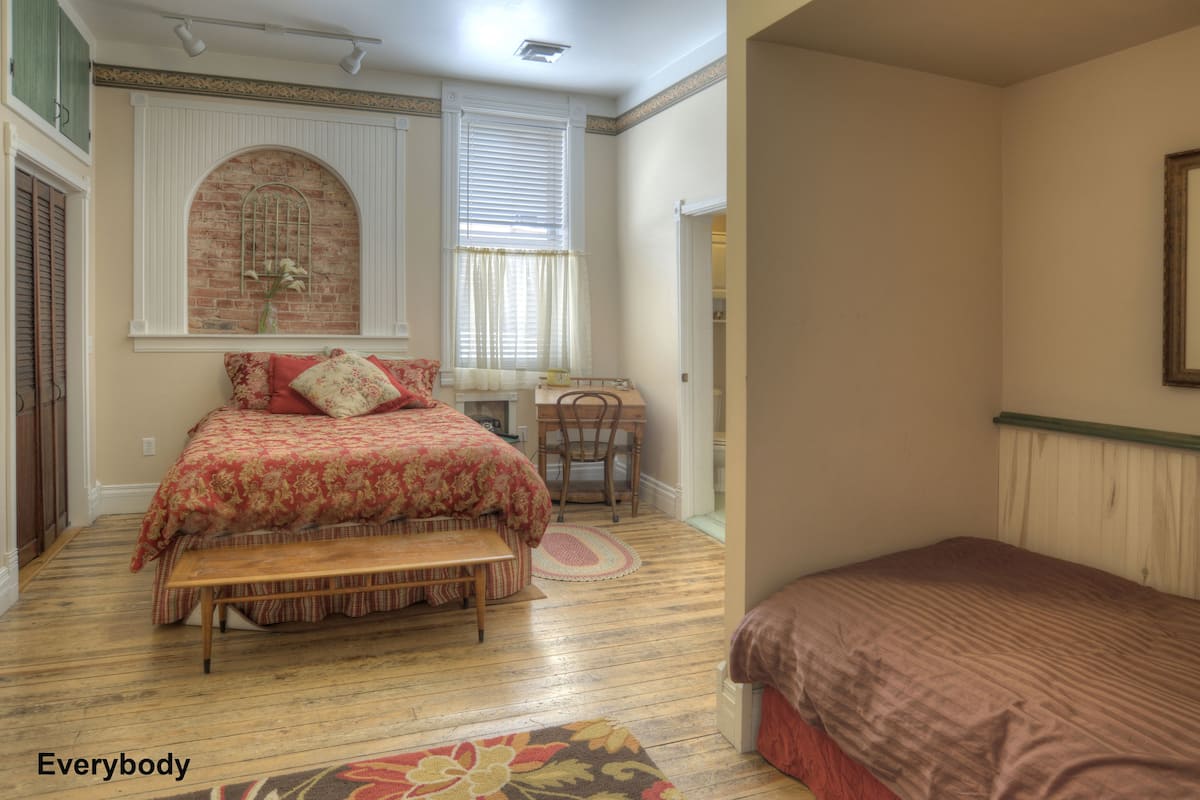 Une chambre avec un grand lit, un plus petit lit, un bureau et une chaise.