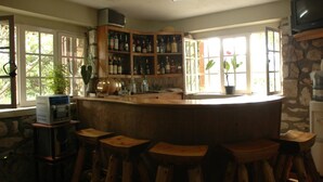 A bar area with wooden stools, a counter with bottles, and a television on a stone wall. - Ranch Le Montcel (Carrefour)