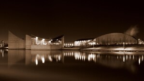 A nighttime view of a modern building with a reflective water body in front. - Airport Lodge Wichita Kansas (Wichita)