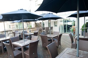 Terrasse mit Sitzgelegenheiten, Tischen und Stühlen, beschattet durch Sonnenschirme.