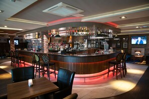 Eine Bar mit einer gebogenen Theke, verschiedenen Sitzgelegenheiten und einem Fernsehbildschirm.