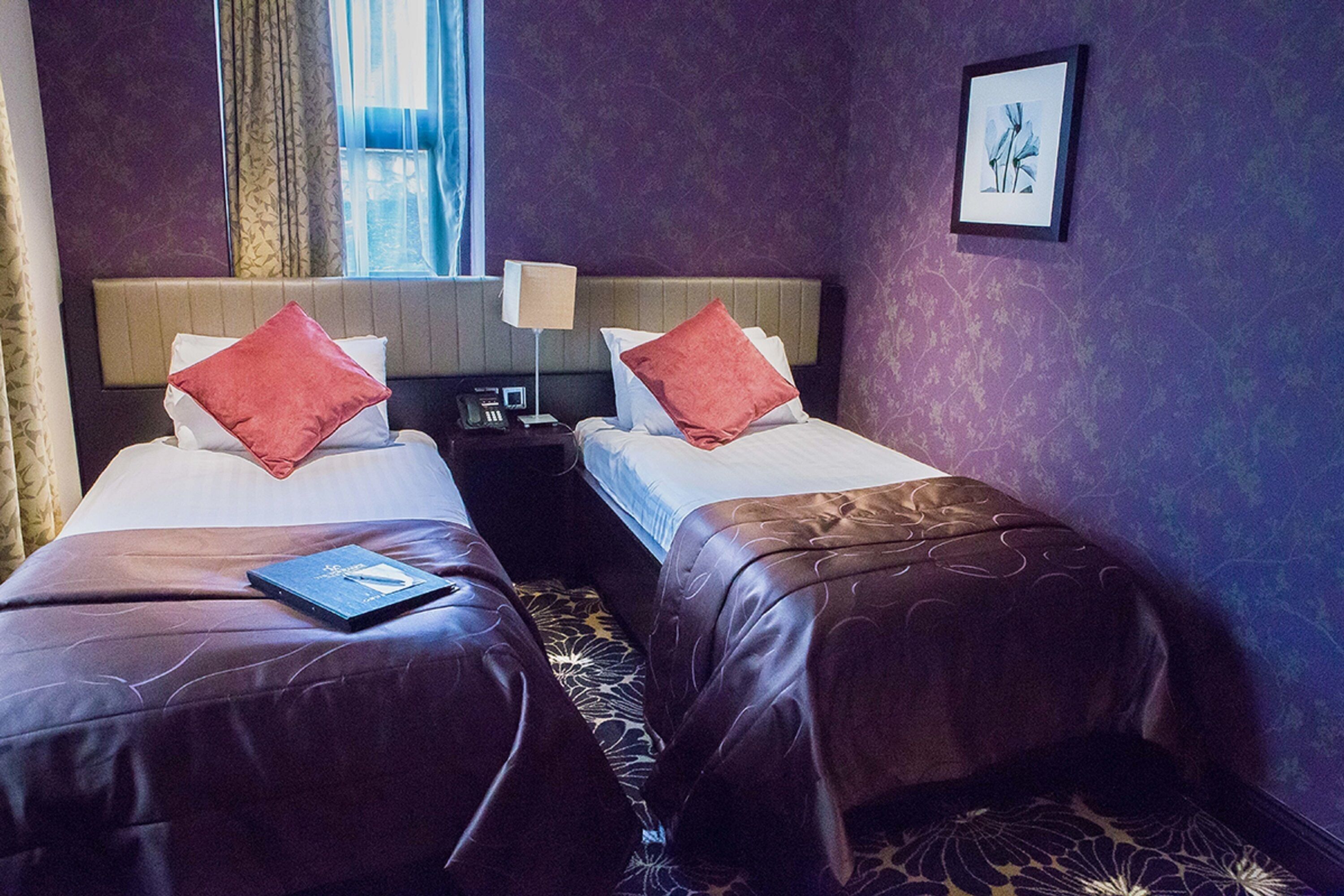 A hotel room with two beds, each with a red pillow and a laptop on one bed.