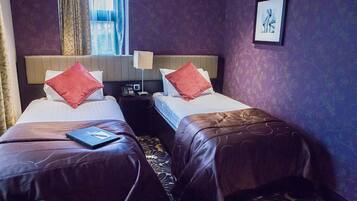 A hotel room with two beds, each with a red pillow and a laptop on one bed.