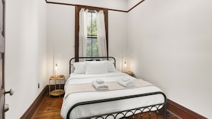 Een slaapkamer met een bed, nachtkastjes, een raam met gordijnen en een houten vloer.