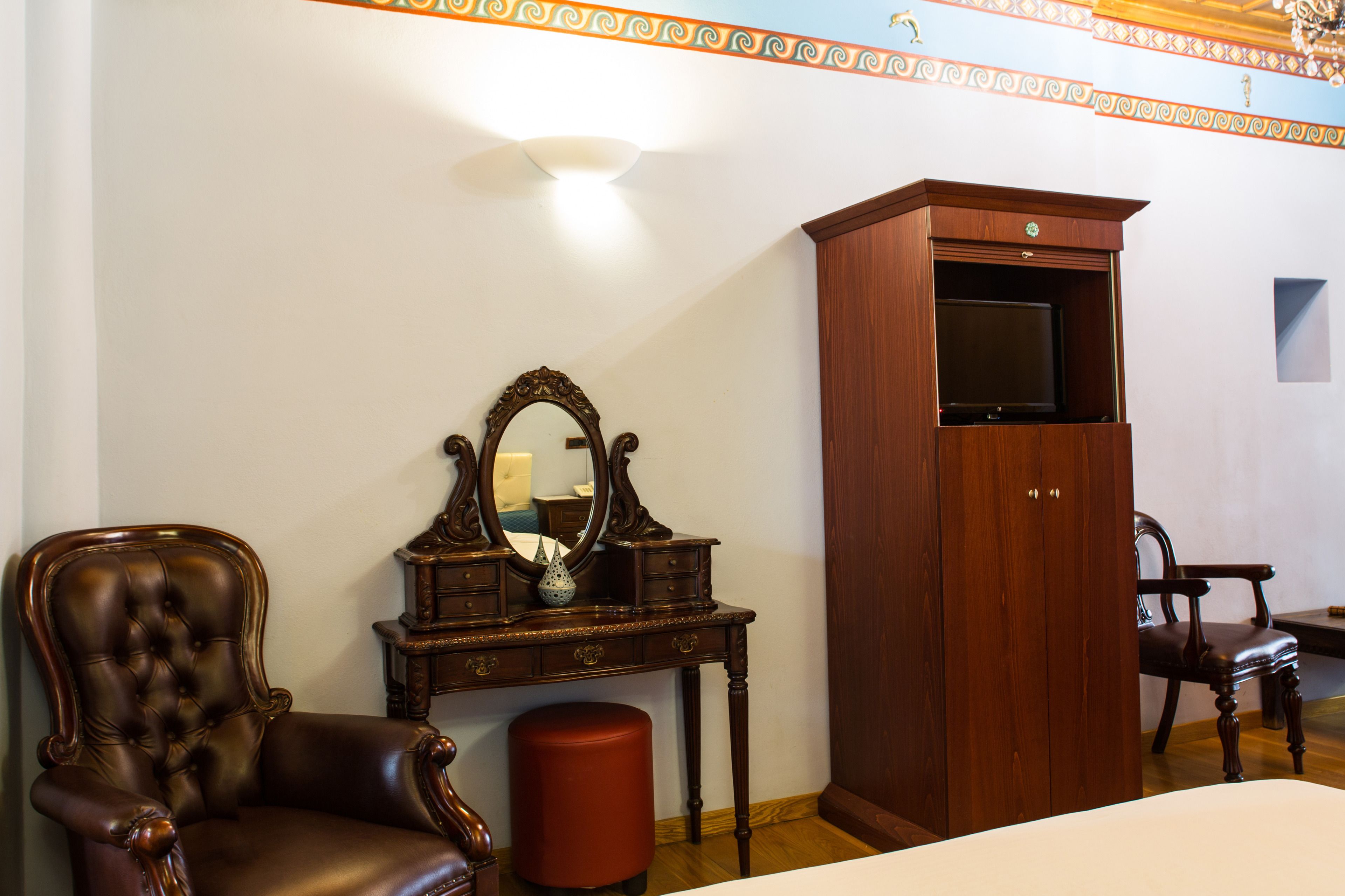 A room with a wooden cabinet, a mirror, a chair, and a small stool.