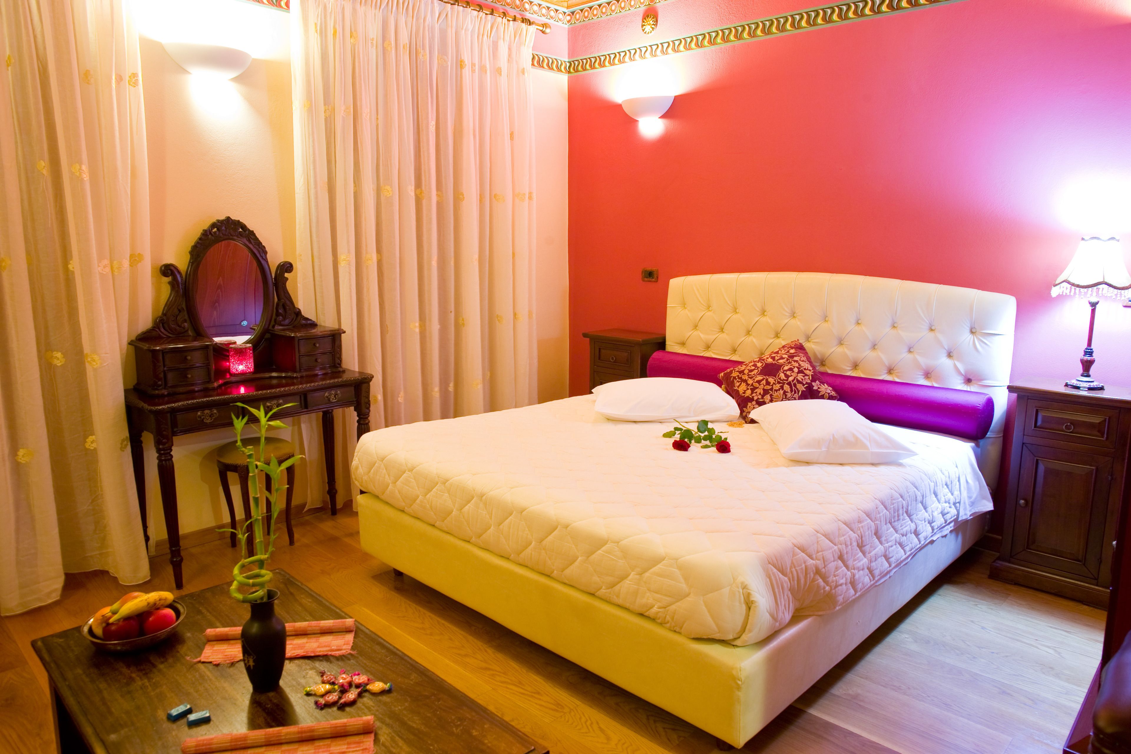 Un dormitorio ordenado con una cama, un tocador con espejo y una mesita con un florero y adornos.