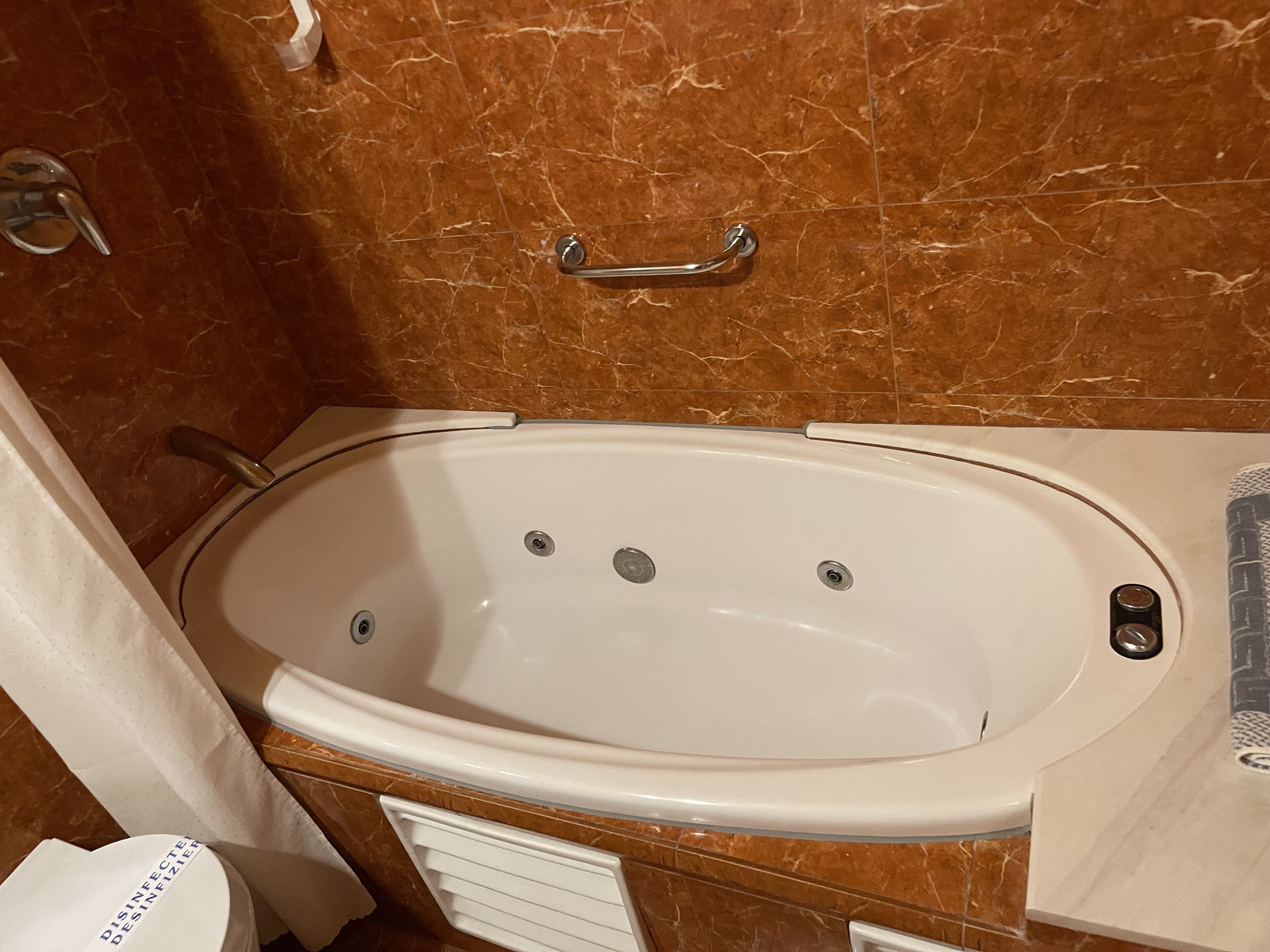 Une salle de bain avec un mur en marbre, une baignoire blanche, un porte-serviettes et un rideau de douche.
