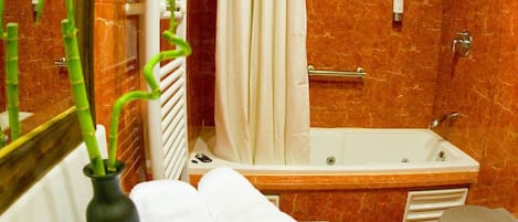 A bathroom with a marble wall, a bathtub, a toilet, a sink, a mirror, and a plant in a vase.