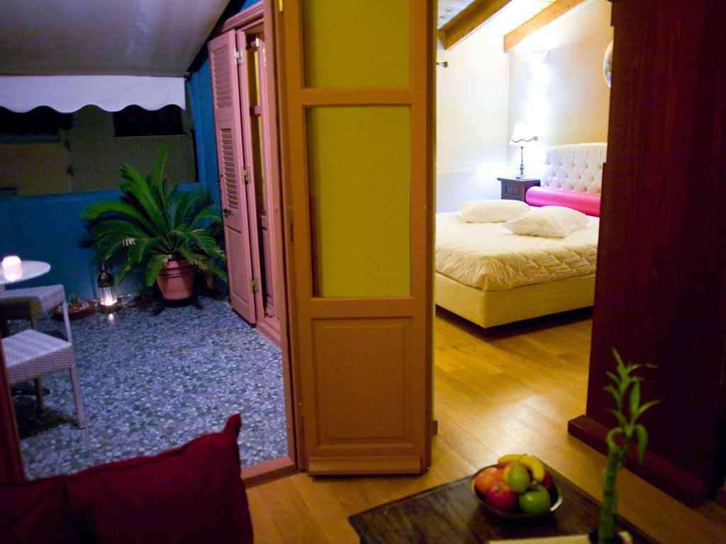 A room with a bed, a small table with fruit, a potted plant, and a door leading to another room.