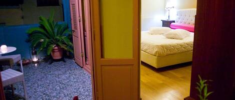 A room with a bed, a small table with fruit, a potted plant, and a door leading to another room.