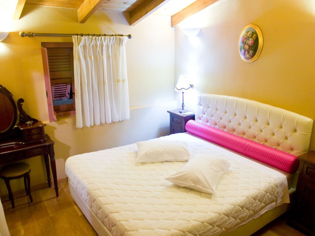A bedroom with a large bed, a bedside table with a lamp, a wooden desk, and a mirror.