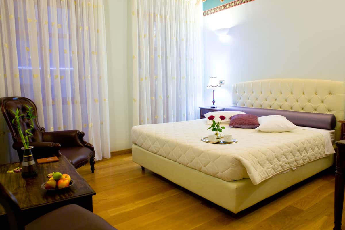 A neatly arranged hotel room with a large bed, a wooden coffee table, a chair, and a vase with flowers.