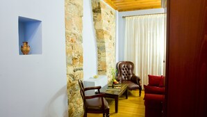 Ein Zimmer mit Steinwand, Holzboden, Ledersessel, rotem Sofa, Couchtisch aus Holz und einer Vase auf einem weißen Tisch.