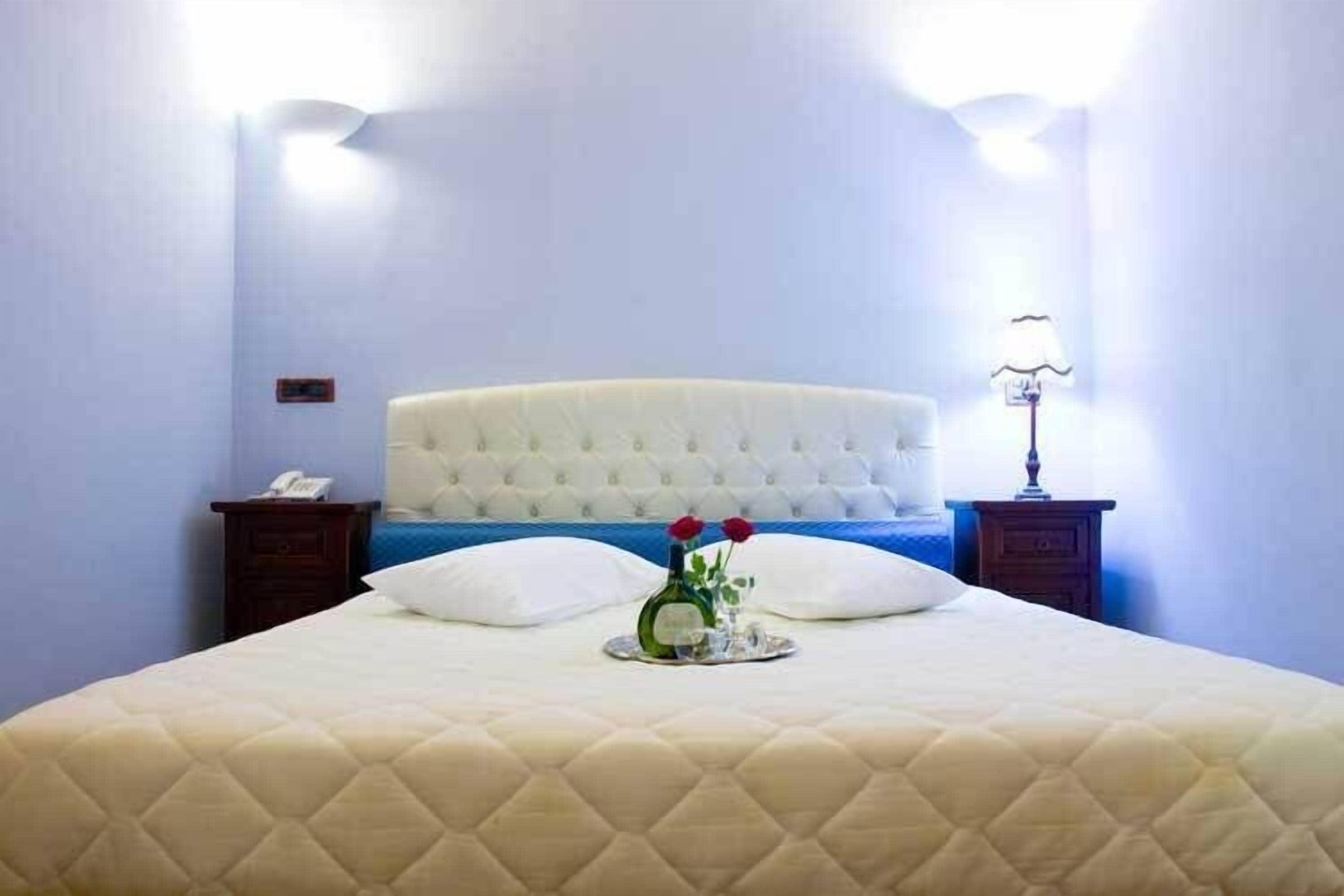 A neatly made bed with a quilted cover, a bedside table with a lamp, and a vase with flowers on the bed.