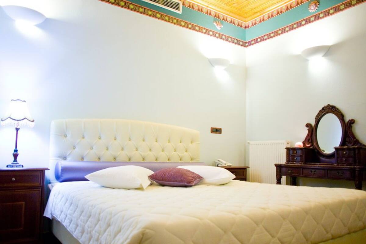 A bedroom with a large bed, a nightstand, a dresser with a mirror, and a lamp.