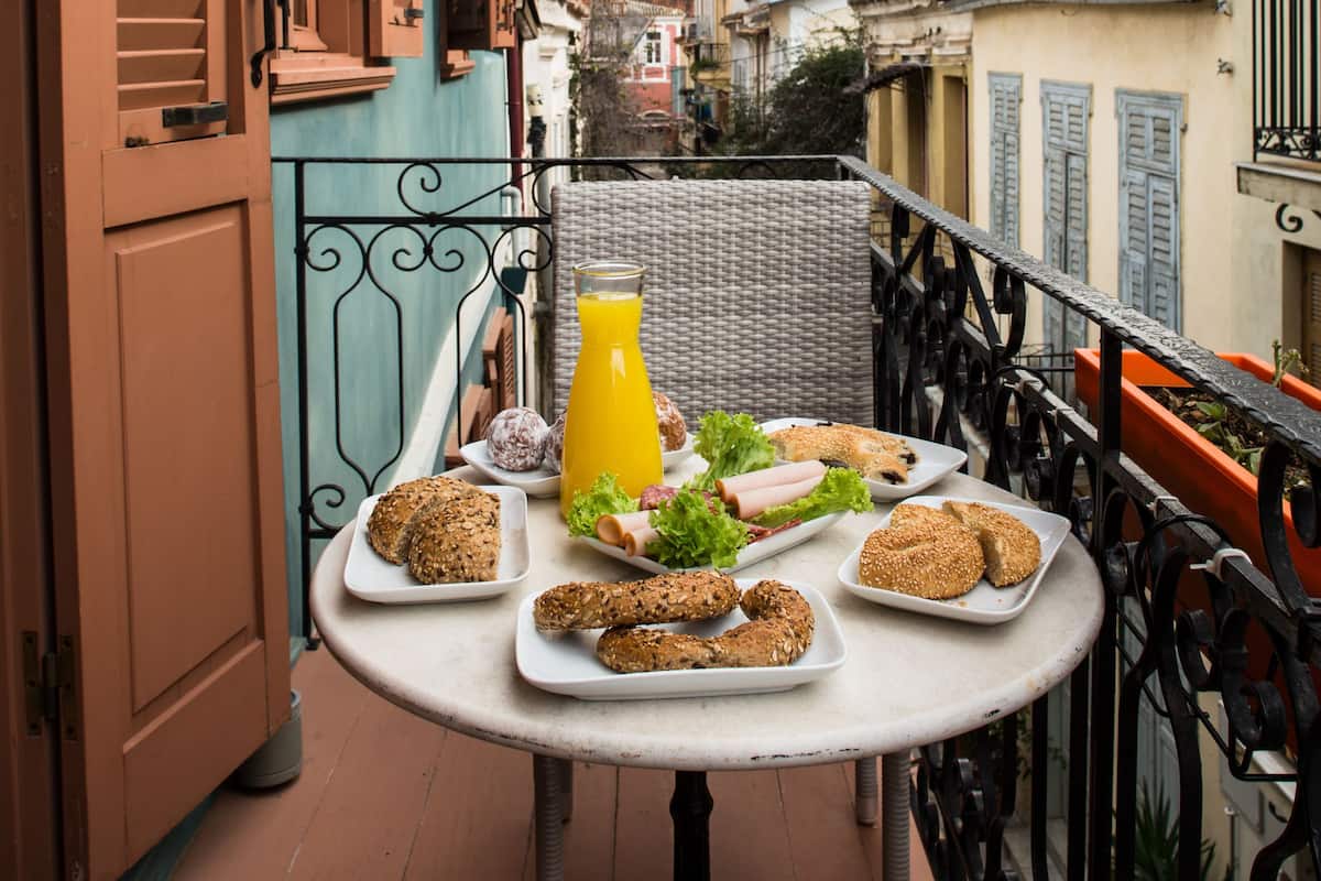 A balcony with a table set with food and a drink, overlooking a cityscape.