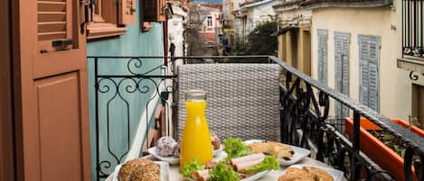 A balcony with a table set with food and a drink, overlooking a cityscape.