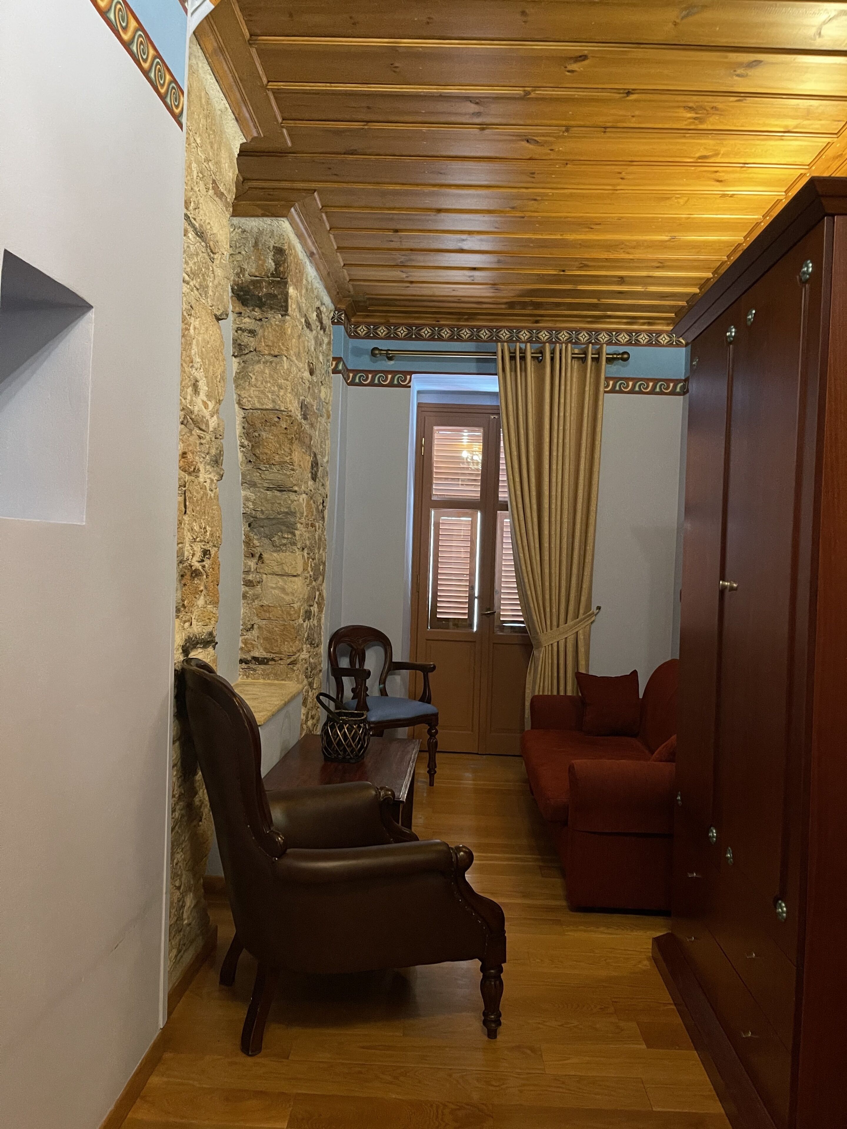 A room with a stone wall, wooden ceiling, a wooden door, a red sofa, a wooden chair, and a small table.