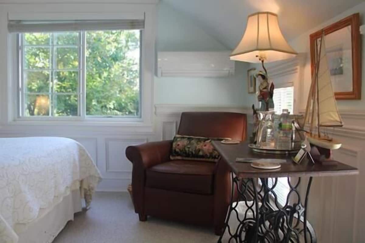 Une chambre à coucher avec un lit, une chaise, une table avec une lampe et une fenêtre donnant sur un paysage verdoyant.