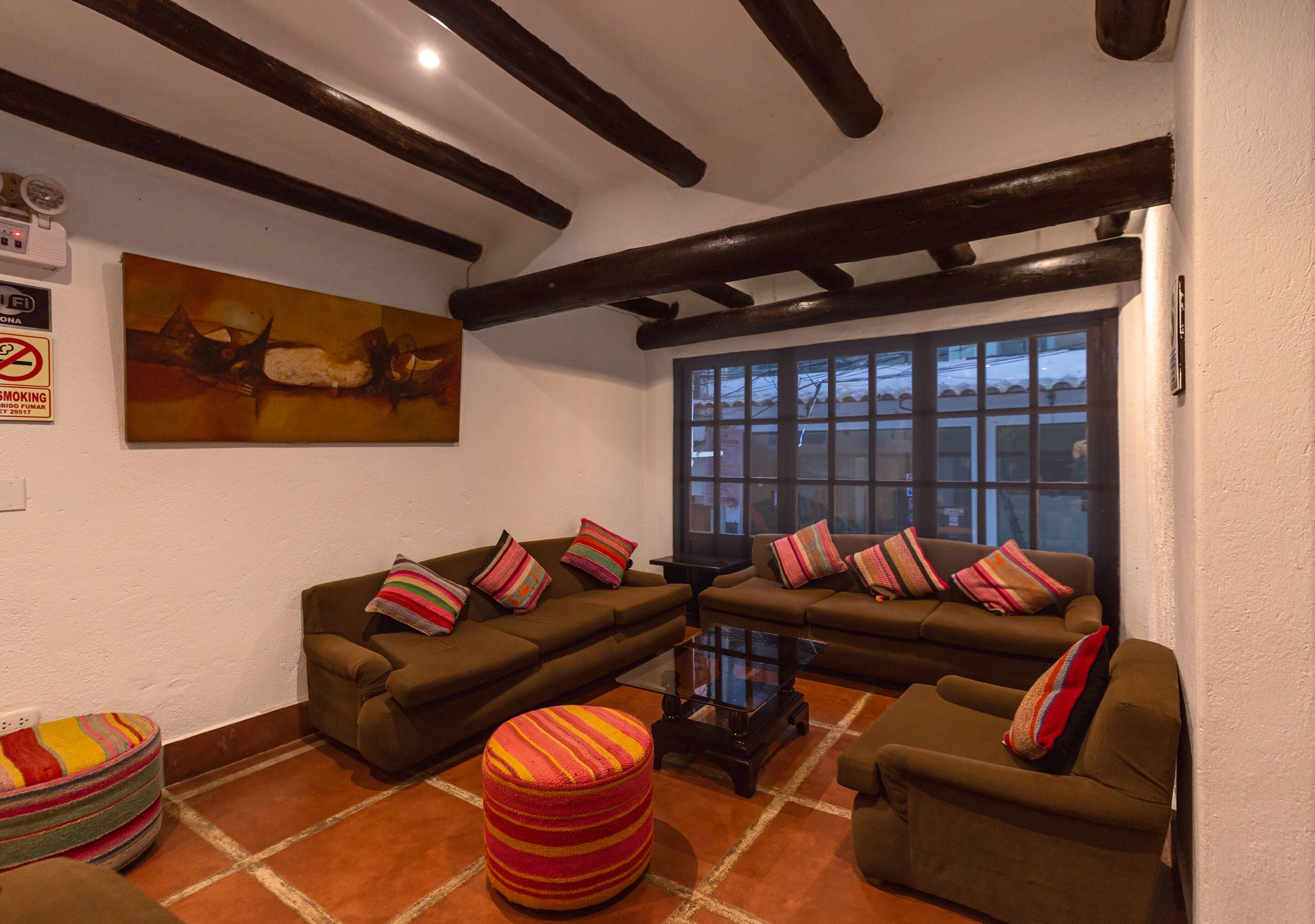 A cozy living room with two sofas, a coffee table, and a colorful ottoman. There is a painting on the wall and a window with a view of the outside.