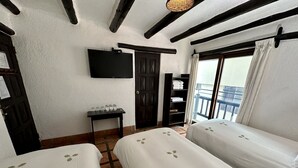 Habitación de hotel con dos camas, un televisor montado en la pared, una mesita con vasos, un armario y un balcón con vistas.