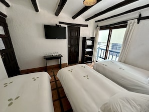Habitación con dos camas, televisión montada en la pared, una mesita con vasos, armario y balcón con vistas.