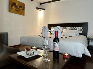 A hotel room with a neatly made bed, a dining table with a dessert and wine, and a bedside table with a candle. - Hatun Inti Classic (Machu Picchu)