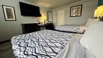 A hotel room with two beds, a flat-screen TV mounted on the wall, a desk with a lamp, and framed artwork on the walls.