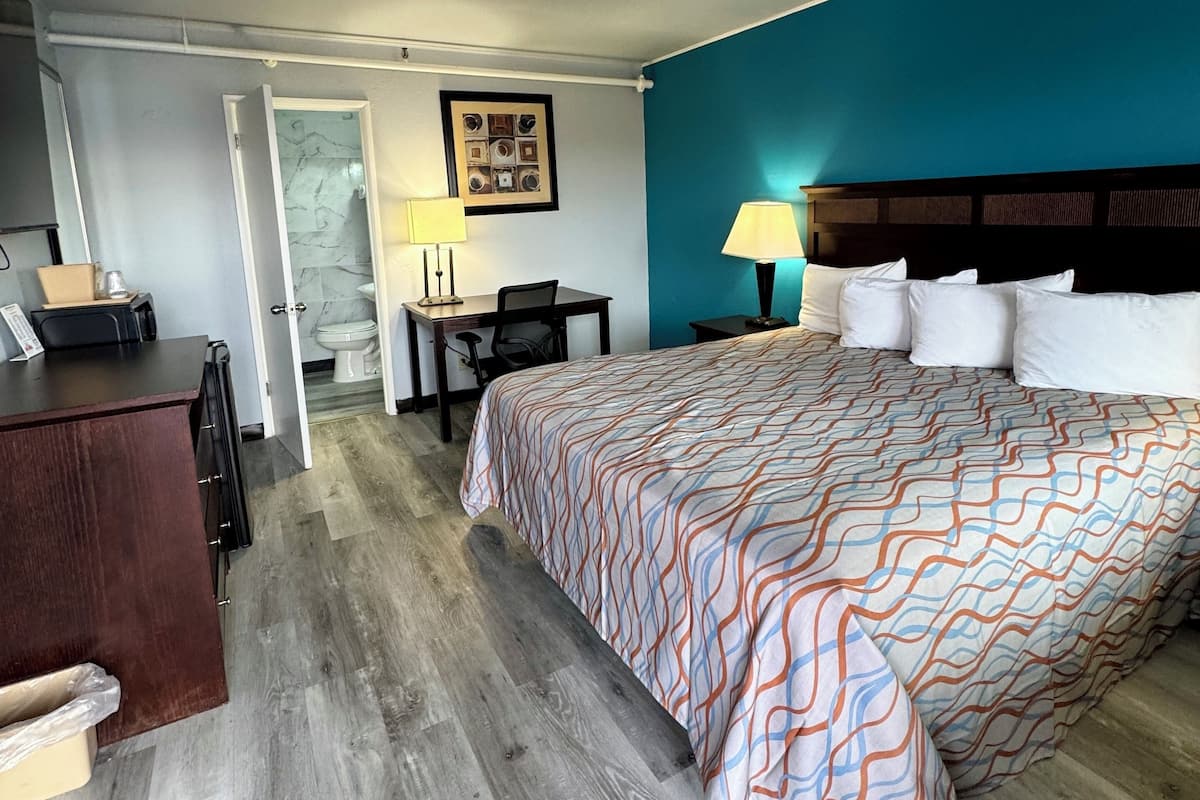 A hotel room with a large bed, a desk, a chair, and a bathroom visible through an open door.