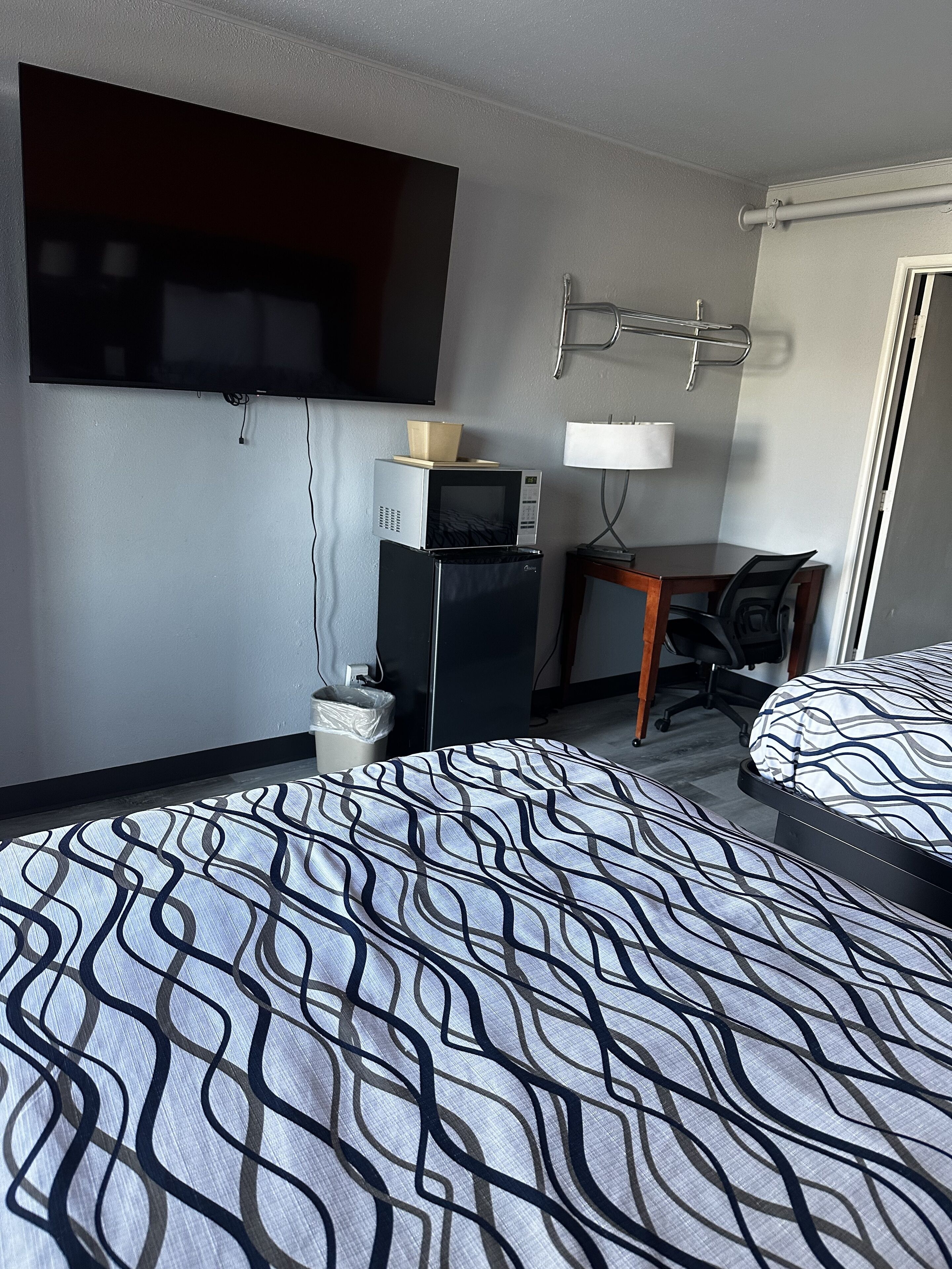 A hotel room with a bed, a desk, a television, a microwave, and a trash bin.