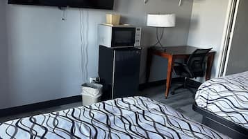 A hotel room with a bed, a desk, a television, a microwave, and a trash bin.