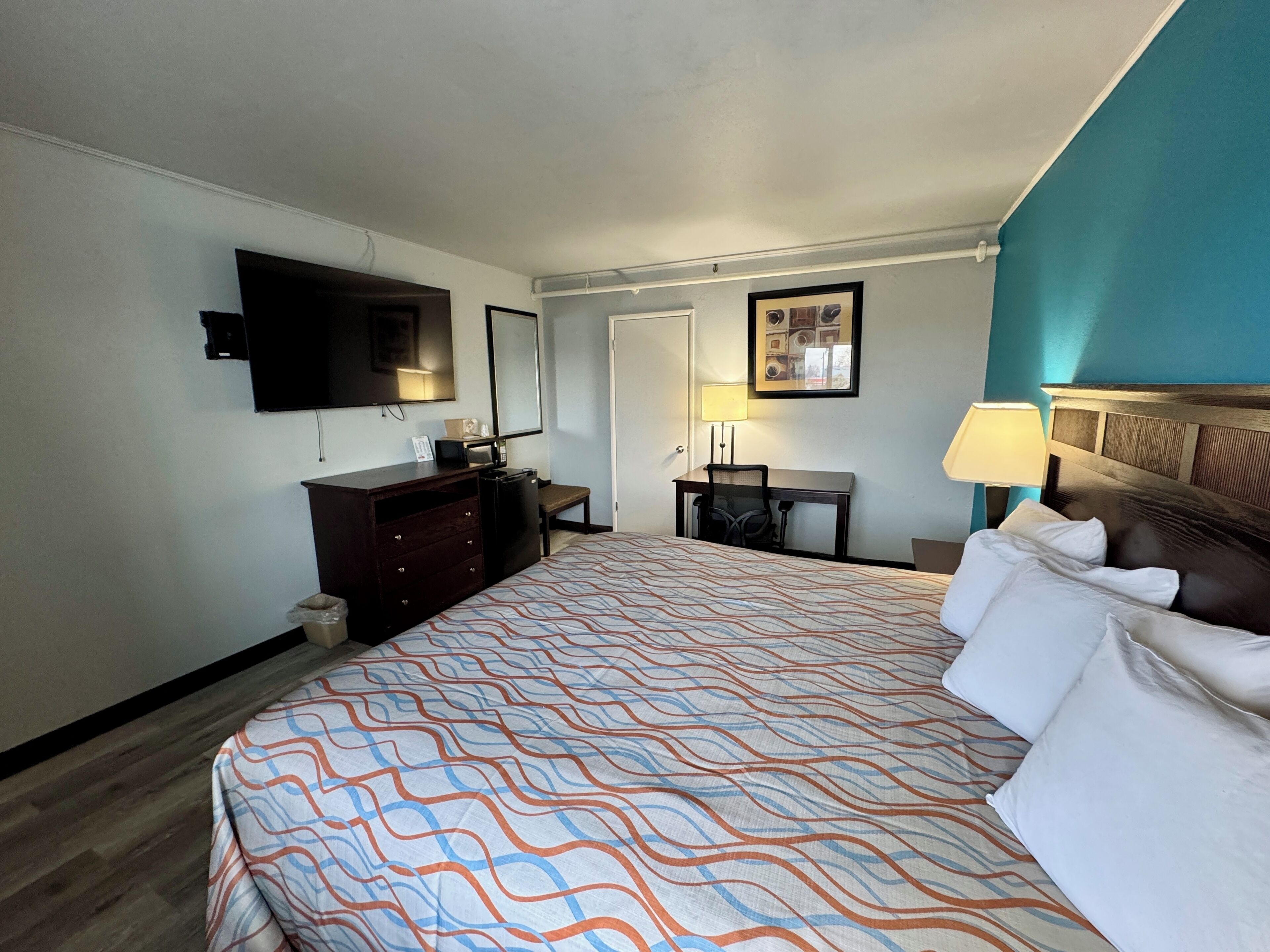 A hotel room with a bed, a desk, a television, a dresser, and a door.