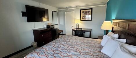 A hotel room with a bed, a desk, a television, a dresser, and a door.