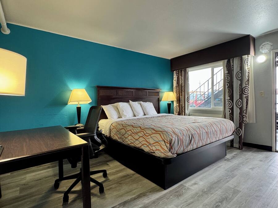 Una habitación de hotel con cama, escritorio, silla y ventana con cortinas.
