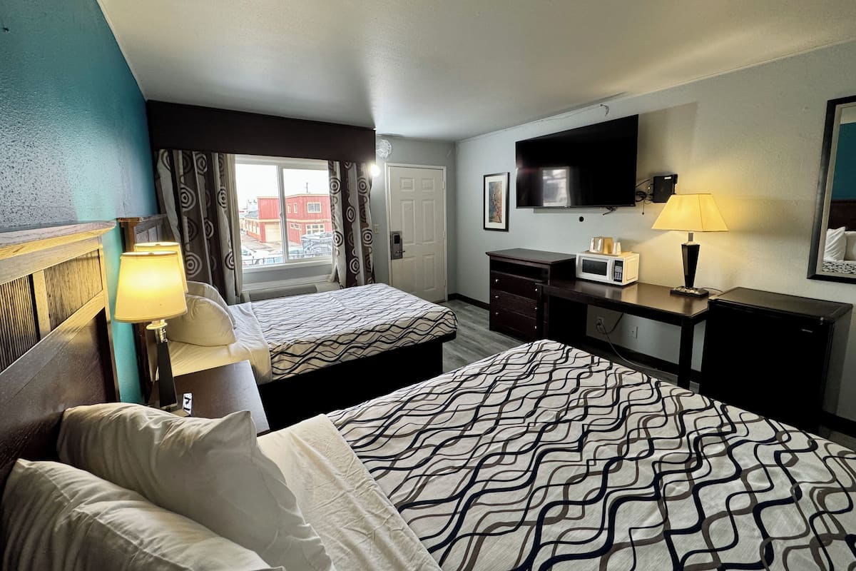 A hotel room with two beds, a desk, a TV, and a window with curtains.