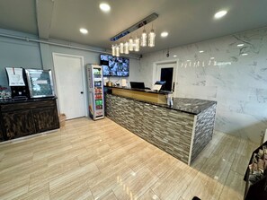 A hotel reception area with a marble counter, a coffee machine, a Red Bull vending machine, and a flat-screen TV. - Nampa Downtown Inn (Nampa)