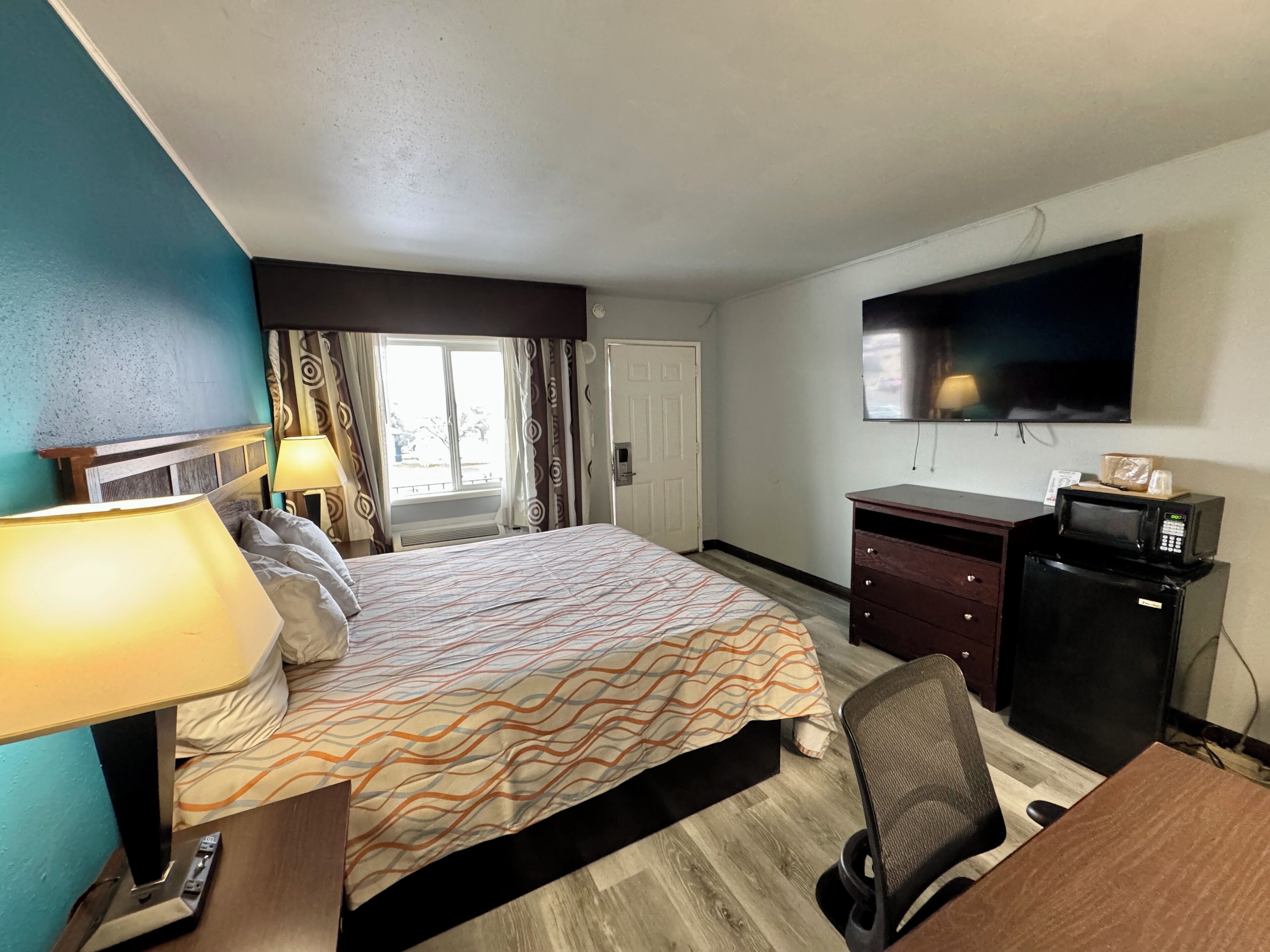 A hotel room with a bed, desk, chair, TV, and a window with curtains.