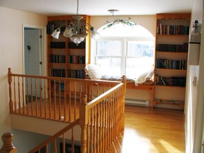 A spacious room with a wooden staircase, a large window with a view, and a bookshelf filled with books. - New Horton Lake Inn (New Horton)