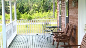 Eine Holzterrasse mit weißer Geländer, einem Tisch mit Stühlen und Blick auf ein bewaldetes Gebiet.