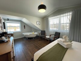 Quarto com uma cama grande, área de estar com uma cadeira, banheira e janela com cortinas.