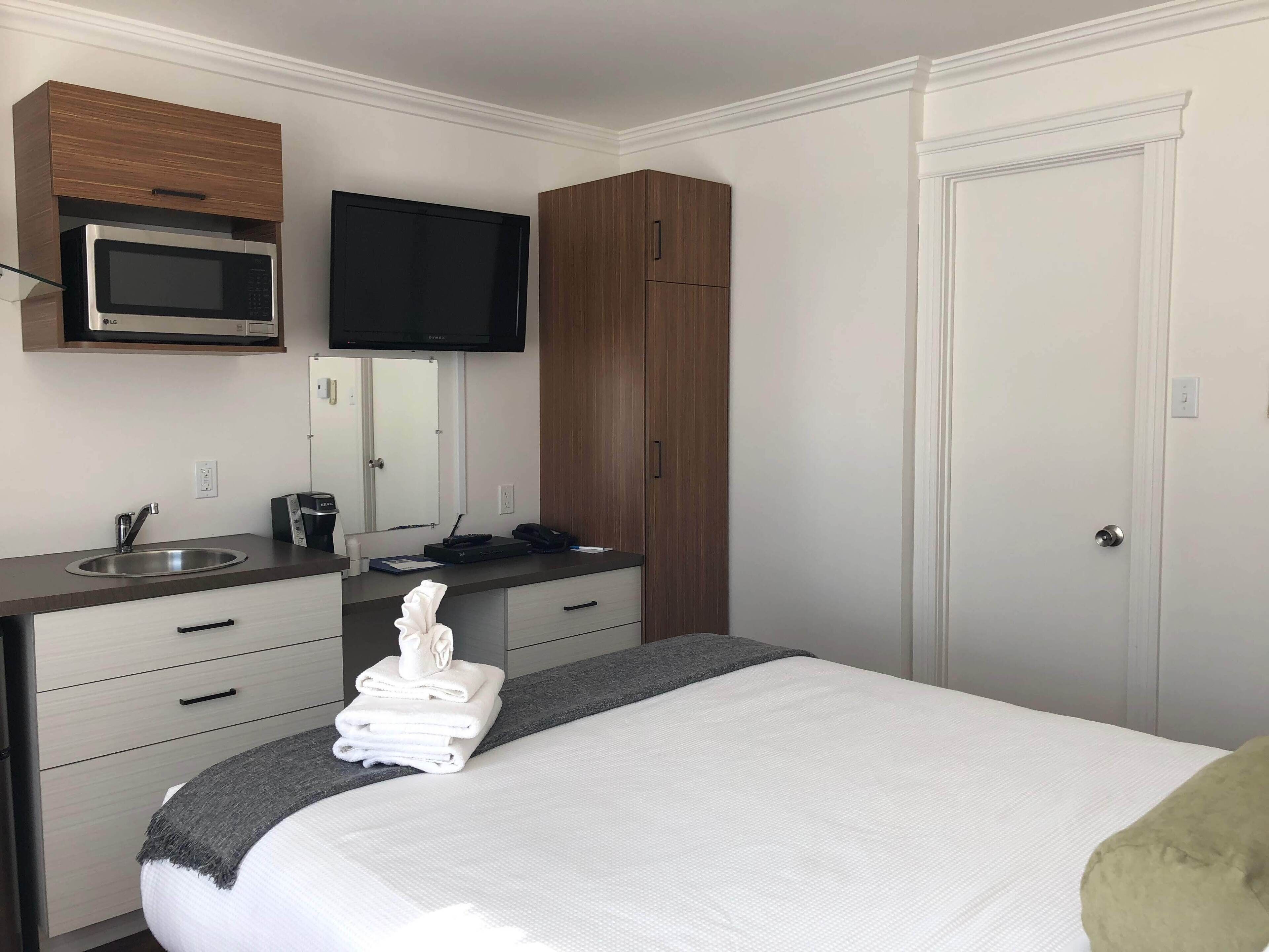A hotel room with a bed, a flat-screen TV mounted above the dresser, a microwave, a sink, and a wardrobe.