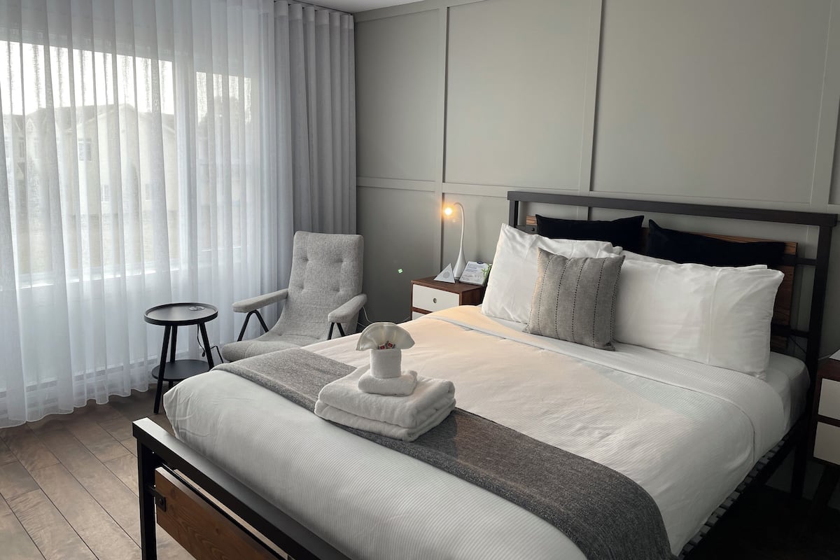 A hotel room with a bed, a chair, a nightstand, and a lamp.