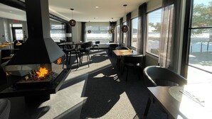 Un espace de restauration intérieur moderne, doté d’un poêle à bois, de grandes fenêtres et de mobilier contemporain.