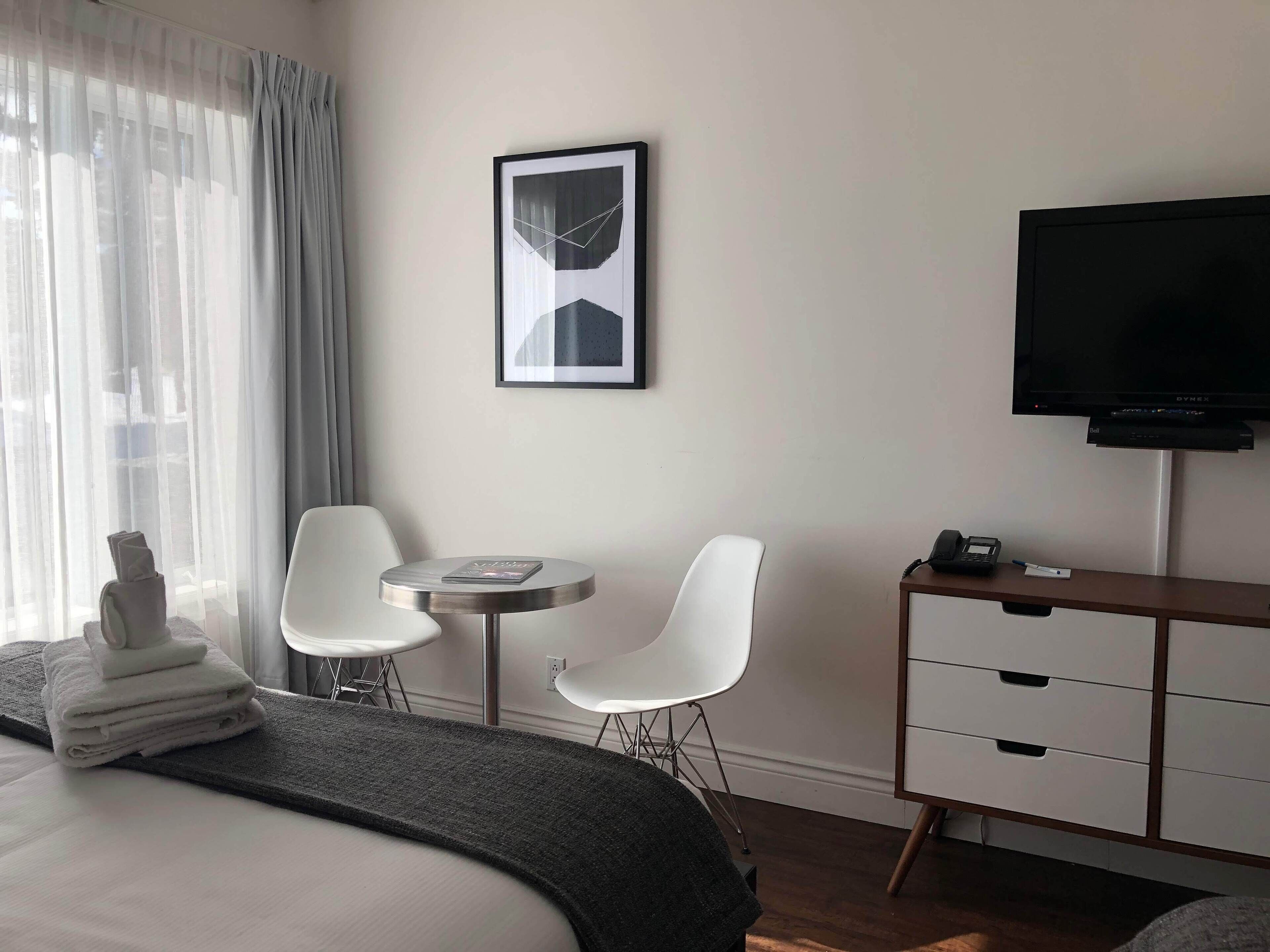A hotel room with a bed, a desk with chairs, a television, and a framed picture on the wall.